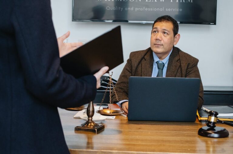 Free Crop unrecognizable employee representing new case details to concentrated middle aged ethnic lawyer sitting at table with laptop gavel and justice scales Stock Photo